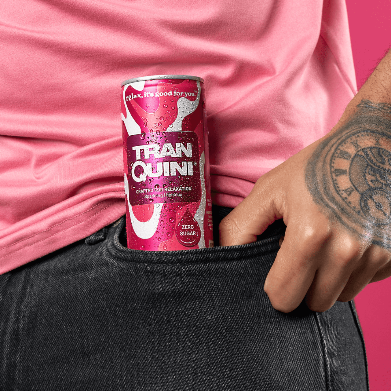 A person with a tattooed arm casually slips a pink can of "Tranquini" labeled "Zero Sugar" into their black jeans pocket. Wearing a coordinating pink shirt against a matching background, they showcase the can's label: "Relax, it's good for you." This scene radiates effortless style and ease, inviting you to join the subscription.